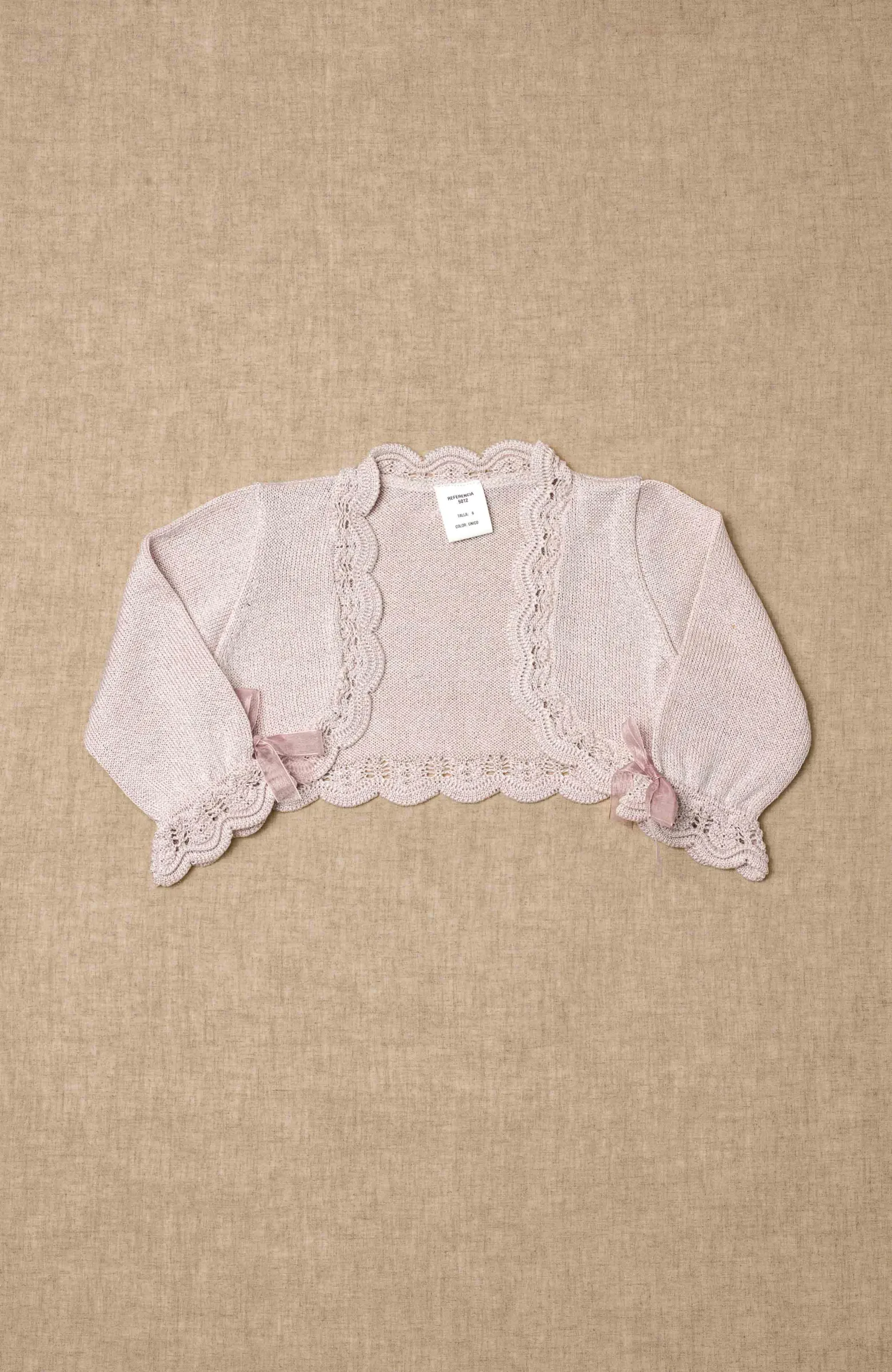 Chaqueta de ceremonia rosa metalizado para niña con detalle de ondas en el bajo y lacitos de organza,ideal para ceremonia infantil.